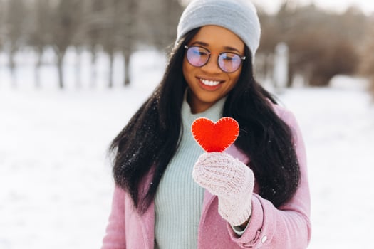 Young African American woman with glasses and warm mittens holding a decorative red heart on Valentine's Day in winter. photo