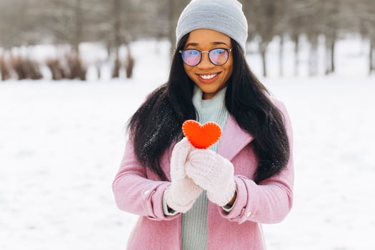 Young African American woman with glasses and warm mittens holding a decorative red heart on Valentine's Day in winter. photo