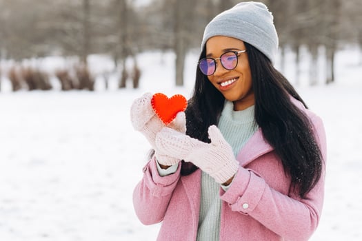 Young African American woman with glasses and warm mittens holding a decorative red heart on Valentine's Day in winter. photo