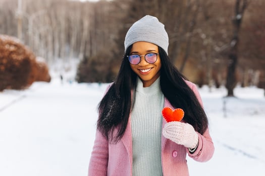 Young African American woman with glasses and warm mittens holding a decorative red heart on Valentine's Day in winter. photo