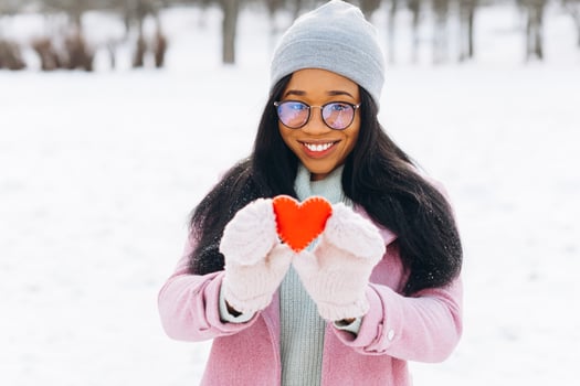 Young afro american woman with glasses and warm mittens holding a decorative red heart on Valentine's Day in winter. photo
