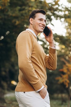 Modern handsome smiling man in yellow and white clothes talking on the phone in the park at sunset photo