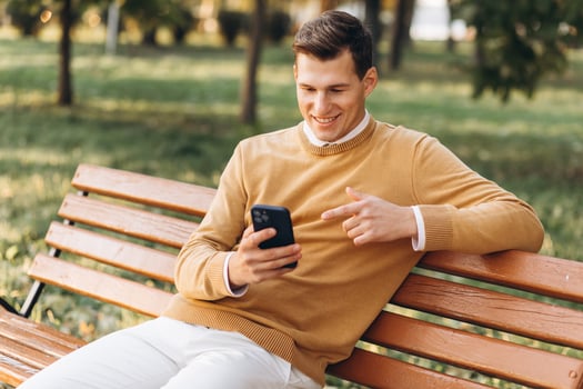 Modern handsome smiling man in yellow and white clothes talking on the phone sitting on a park bench at sunset photo