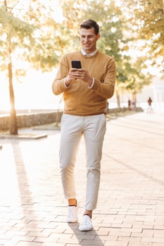 Modern handsome smiling man in yellow and white clothes talking on the phone in the park at sunset photo