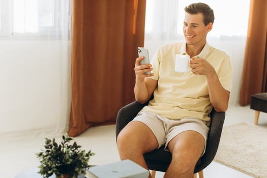 Handsome young man in yellow casual clothes sitting at home reading a message on the phone photo