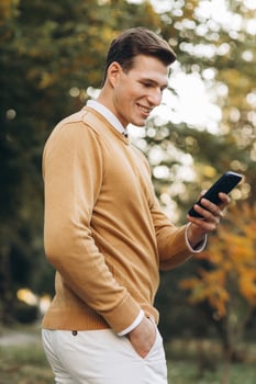 Modern handsome smiling man in yellow and white clothes talking on the phone in the park at sunset photo