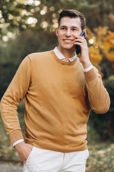 Modern handsome smiling man in yellow and white clothes talking on the phone in the park at sunset photo