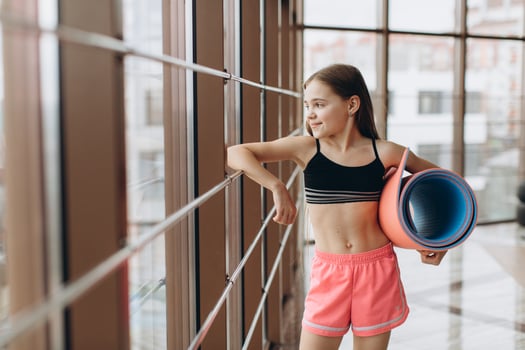 Charming little girl holding fitness mat and smiling while doing yoga in fitness hall photo