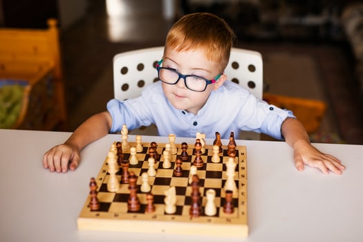 Ginger boy with down syndrome with big glasses playing chess at home photo
