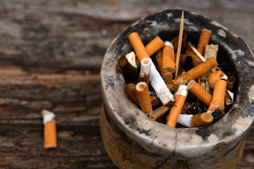 Closeup of an ashtray filled with numerous cigarette butts on a wooden surface, symbolizing smoking habits and litter, smoking harm, urban pollution, unhealthy lifestyle, littering. photo