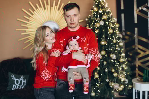 Happy family mom dad and little daughter in red traditional Christmas clothes spending time together near Christmas tree, copy space photo