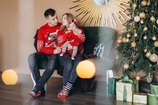 Happy family mom dad and little daughter in red traditional Christmas clothes spending time together near Christmas tree, copy space photo
