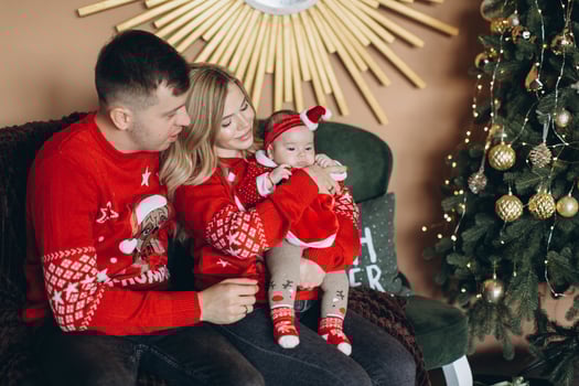 Happy family mom dad and little daughter in red traditional Christmas clothes spending time together near Christmas tree, copy space photo