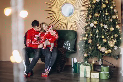 Happy family mom dad and little daughter in red traditional Christmas clothes spending time together near Christmas tree, copy space photo