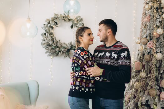 Happy couple in traditional sweater decorating Christmas tree together at home photo