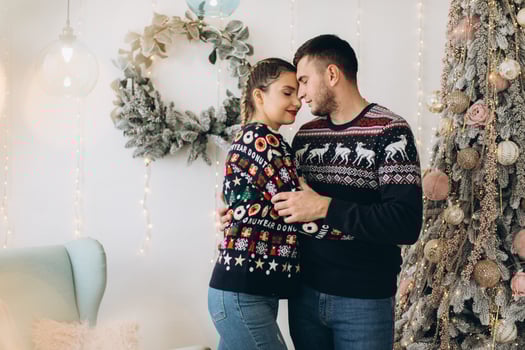 Happy couple in traditional sweater decorating Christmas tree together at home photo