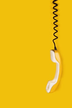 Yellow old phone handset dangles on wire. yellow background vertical banner poster copy space photo