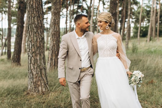 Wedding couple bride and groom walk hand in hand through a pine forest, sunlight filtering through the trees, highlighting their joyful expressions. photo