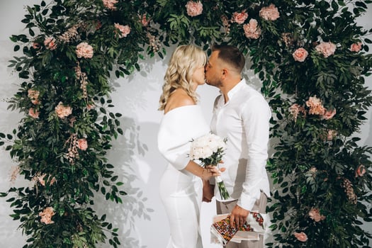 Romantic Wedding Ceremony with Couple Kissing Under Floral Arch in Elegant White Attire photo