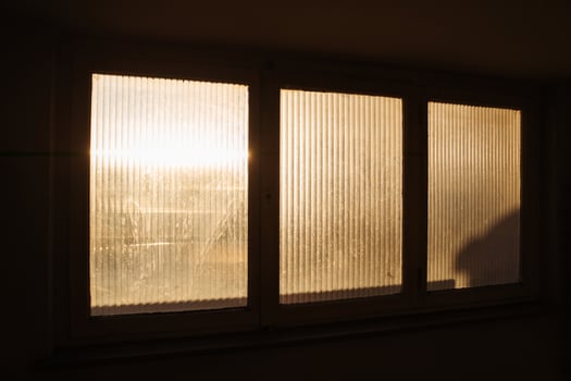 Warm morning sunlight filters through a frosted window, casting soft glows and shadows in apartment building. A serene depiction of peaceful beginnings and tranquil home environments. photo