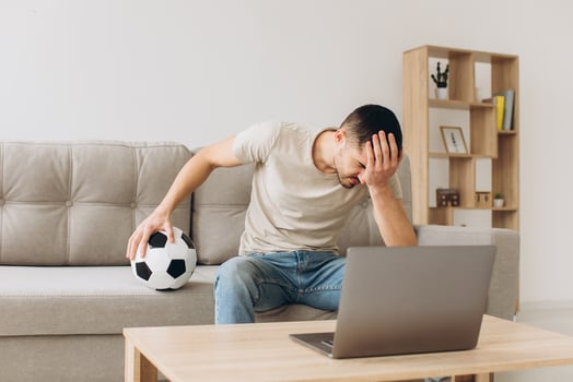 A man sits on a sofa in the living room holding a ball and cheers for the football team watching a match on a laptop photo