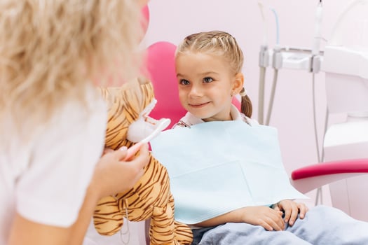 Little girl on a visit to the dentist holding a toy and showing how to brush your teeth in a dental clinic photo