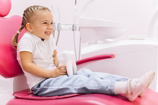 Little girl smiling on a visit to the dentist holding a tooth model at the dental clinic photo