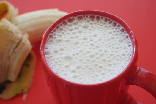 A red cup of milk next to a banana photo