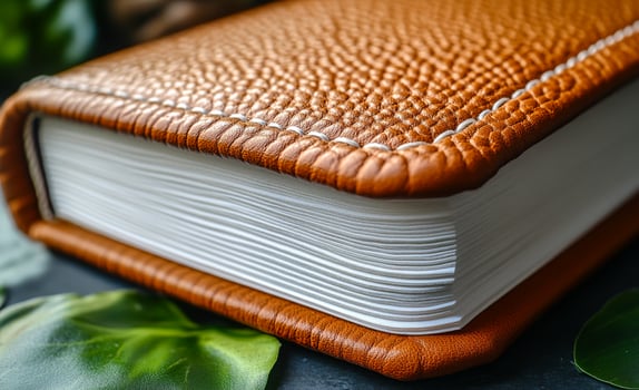 A leather bound book with a white spine and brown cover. The spine is slightly raised and the pages are white. The book appears to be a leather bound journal or diary photo