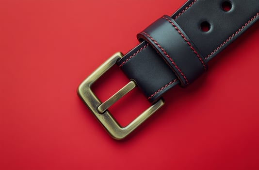 A close-up of a black leather belt with a brass buckle against a smooth red background photo