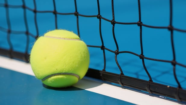 Closeup of tennis ball against blue tennis court with net backdrop photo