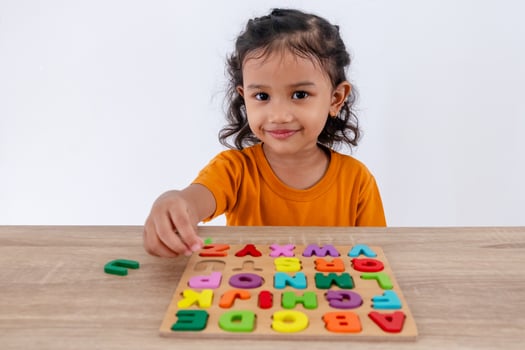 A little Asian girl arranges colorful wooden alphabet letters on a table photo