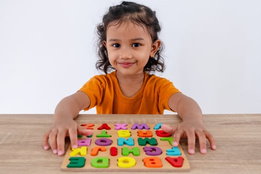 A cheerful little Asian girl plays with wooden alphabet letters on a table photo