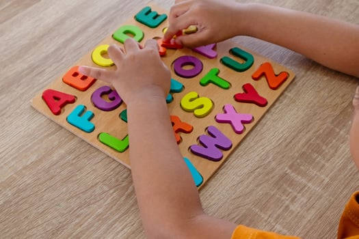 View of a little Asian girl plays with wooden alphabet letters puzzle on a table photo