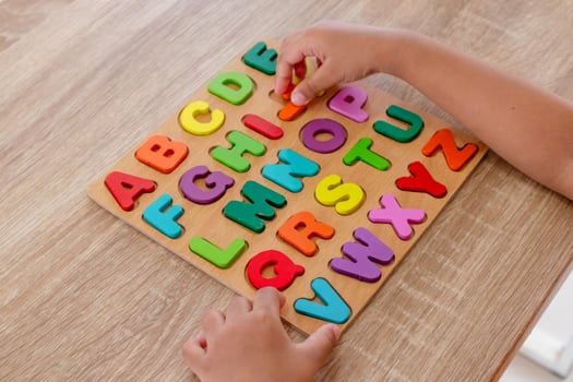Hands of little girl assembles wooden alphabet letters puzzle on a table photo