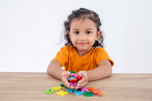 A happy little girl sitting at table with handful of wooden alphabet letters in palm photo