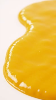 Melted cheese puddle with glossy texture against white backdrop YellowOrange Cheese photo