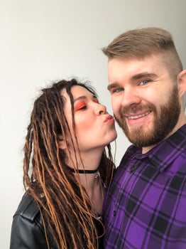 Cheerful Couple Sharing a Playful Moment. Joyful modern rock style female portrait. Woman with dreadlocks and grunge style clothing and make up kissing her boyfriend. photo