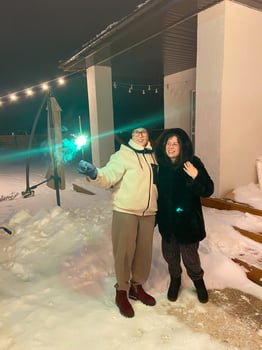 60 year old mother and her 30 year old daughter enjoy a winter night outside a cozy house and celebrating New Year holding a sparkler amidst snow and festive string lights. photo
