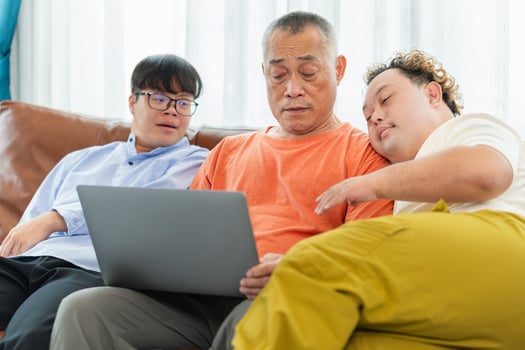 Grandfather and grandson using laptop doing a call in living room, Senior asian man having a good time sitting on couch at home with adult son photo
