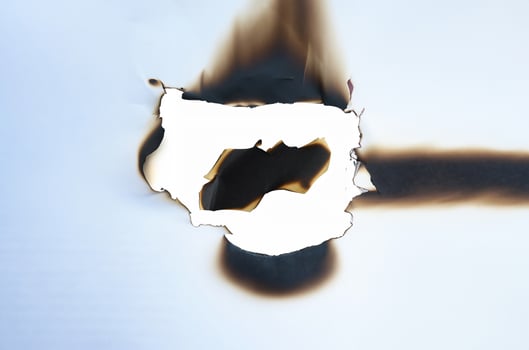 A burnt hole in white paper with irregular scorched edges and slight smoke marks, ideal for use in design projects or as a texture element. photo