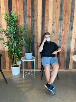Bearded man in casual attire sits on a chair, holding a cup of coffee, against a stylish wooden wall with potted plants. Relaxed and modern atmosphere, perfect for enjoying a peaceful moment photo