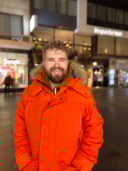 Man walking in a bustling nighttime city street, wearing a bright orange parka. Serene contemplation against the backdrop of lively city lights at night. Urban life concept photo