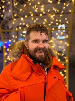 Handsome millennial man model with a hairstyle in winter red parka walks in night city with festive lights. Christmas and winter holidays season photo