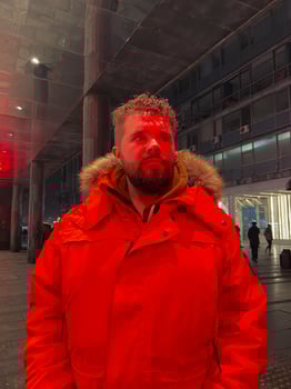 Man walking in a bustling nighttime city street, wearing a bright orange parka. Red neon light. Serene contemplation against the backdrop of lively city lights at night. Urban life concept photo