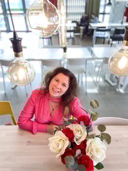 Millennial woman in a vibrant pink sweater sits at table decorated with red and white roses in a modern room. photo