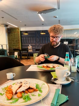 Portrait of a curly handsome man eating at a restaurant and smiling - lifestyle concept. A young man with a beard sitting in a restaurant and going to eat photo