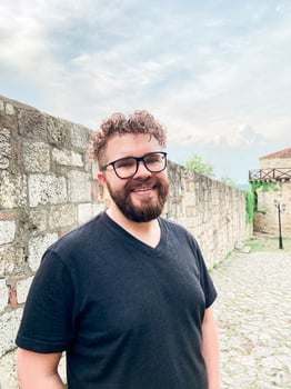 Portrait of millennial attractive man with curly hair hairstyle. Smiling handsome male in casual stylish clothes posing in the street. Cheerful and happy model outdoors. In spectacles, glasses photo
