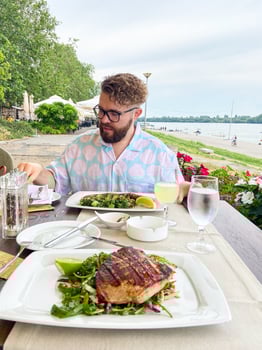 Millennial man enjoying dining with scenic riverside view. Fresh meal and tranquil ambiance provide a perfect setting for a relaxing outdoor dining experience photo