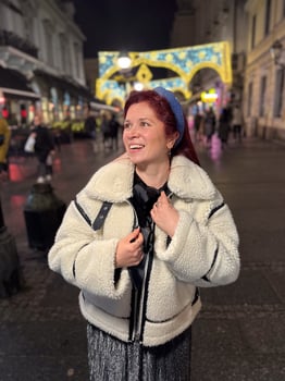 Millennial woman standing outdoors at Christmas night, wrapped in a cozy shearling jacket. the city lights in the background create a warm and Christmas holidays atmosphere, enhancing the peaceful photo